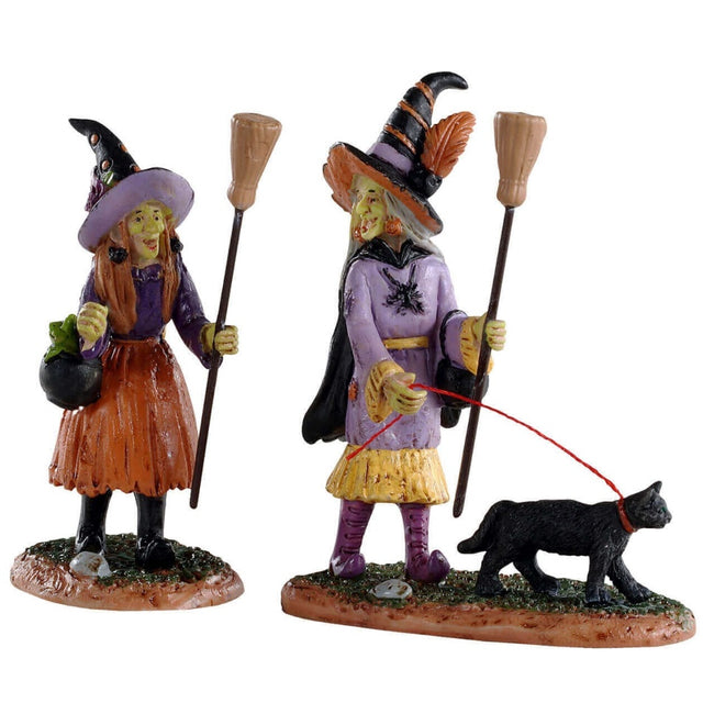Polyresin figurines for a Lemax display. Designed to look like two witches holding brooms going out for a walk. They're both wearing traditional witch hats. One of the witches is walking a black cat on a red leash.
