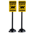 Plastic village accessories for a Lemax display. Designed to look like two yellow signs that read "CAUTION: BLACK CAT CROSSING" and has a cartoon picture of a black cat on it.