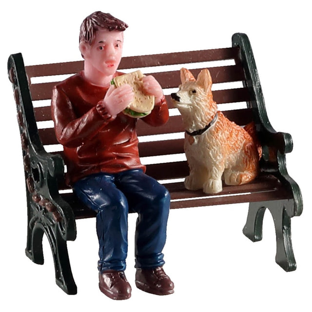 Polyresin figurine for a Lemax Village tabletop display. Designed to look like a man eating a sandwich while sitting on a wooden bench next to a dog