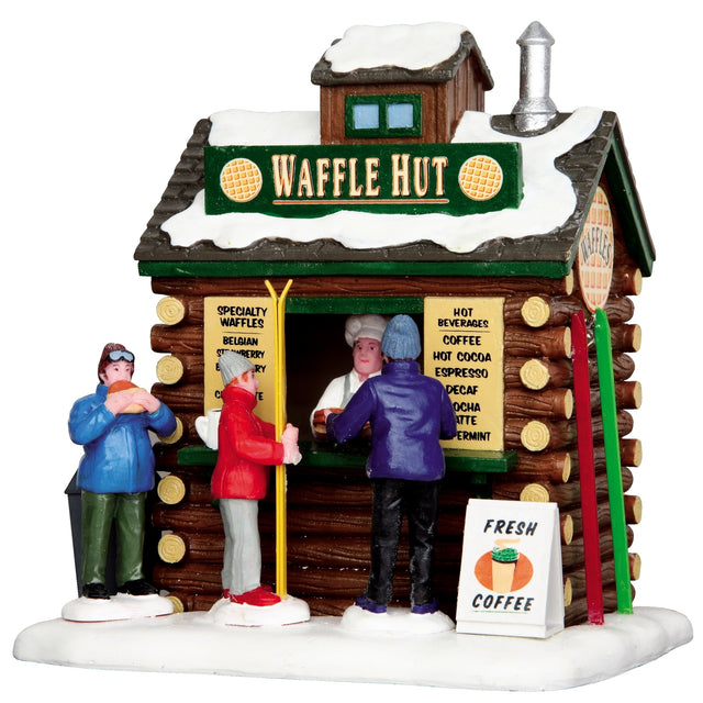 Polyresin building for a Lemax display. Designed to look like a small log cabin covered in snow. The sign on the roof reads "Waffle Hut" and features two waffles. There are three people in line. There are skis leaning up again the side of the cabin. There's a sign on the ground that reads "Fresh Coffee."