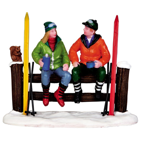 Polyresin figurine for a Lemax display. Designed to look like two people sitting on a wooden fence after a long day of skiing. There's a squirrel sitting on the fence.
