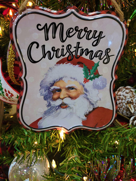 Tin sign hanging on a Christmas tree with other ornaments and ribbons.