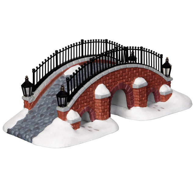 Porcelain lighted building for a Lemax display. Designed to look like a brick bridge with a metal fence. The path on the bridge is made of stone. There's snow on the ground and you can see footsteps in the snow.