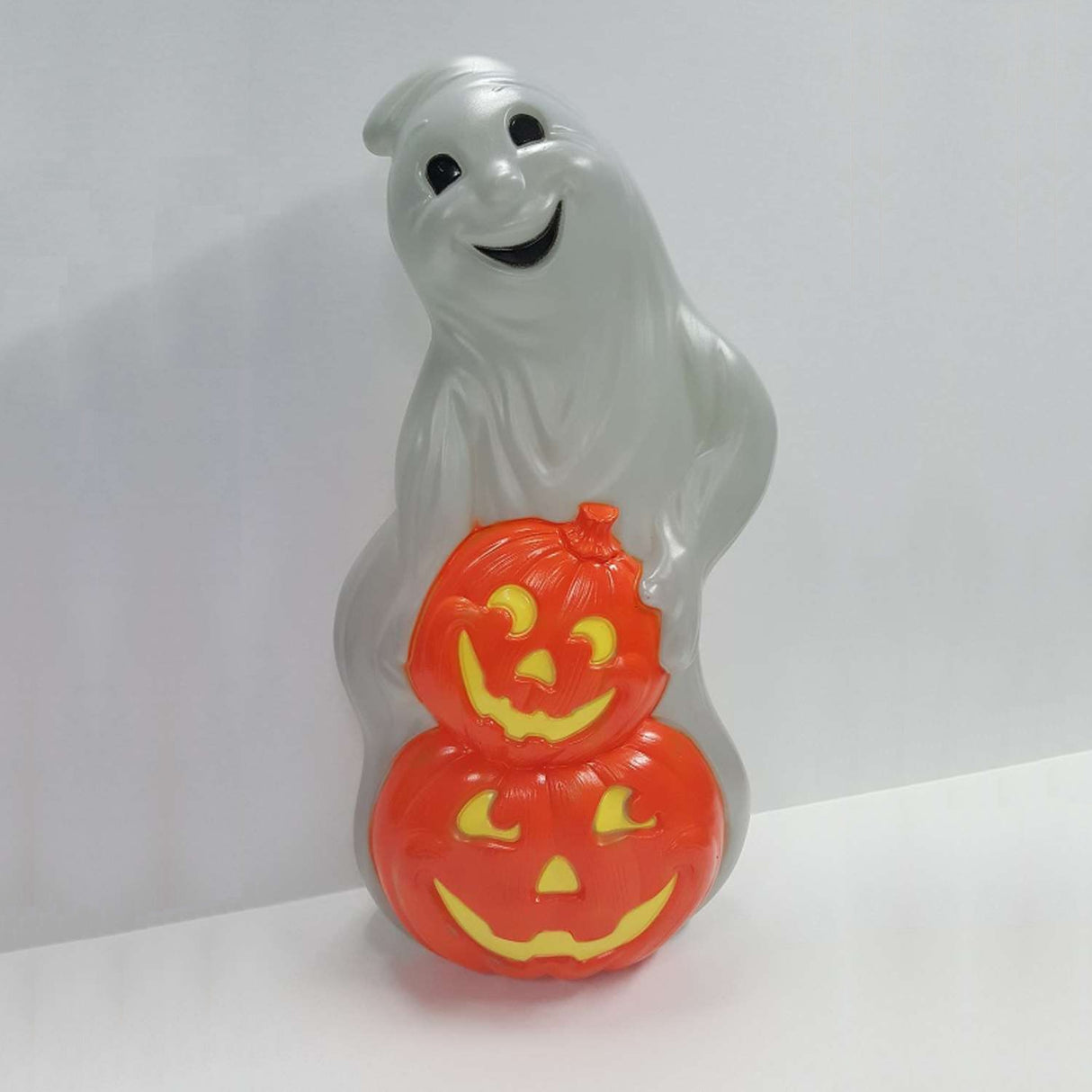 A blow mold Halloween decoration designed to look like a smiling ghost with two carved jack-o-lanterns stacked in front of it.