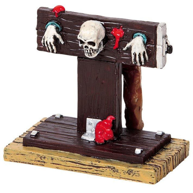 Polyresin figurine for a Lemax display. Designed to look like a skeleton stuck inside a guillotine.