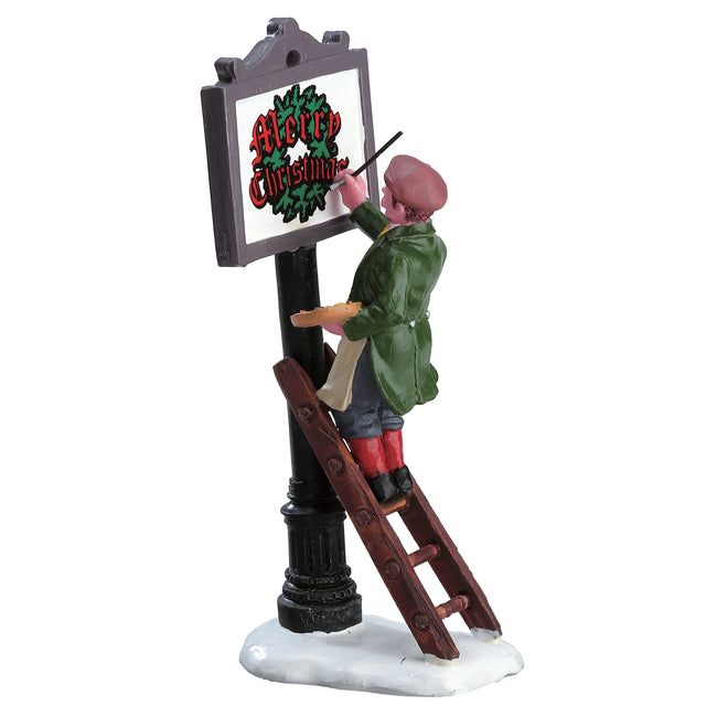 Polyresin figurine for a Lemax display. Designed to look like someone standing on a ladder painting a sign on a pole. The sign reads "Merry Christmas" in red font and there's a green wreath behind it.