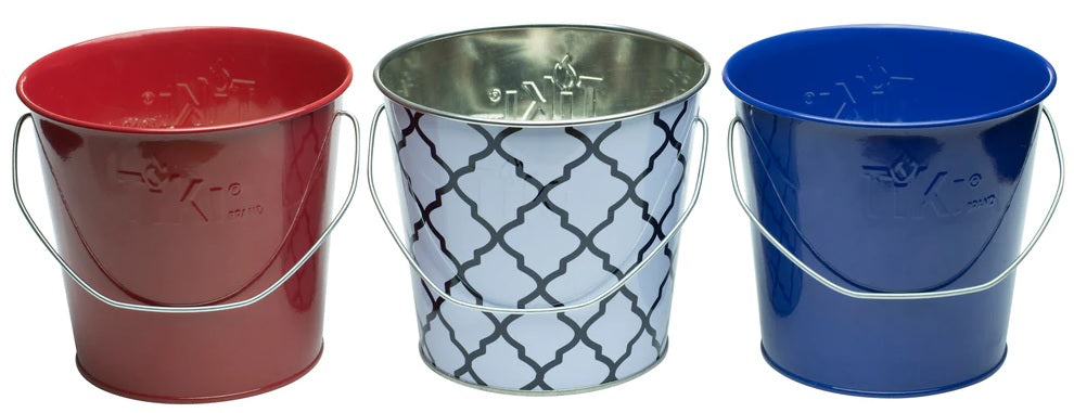 This picture shows the different color options for these TIKI candles. One candle is in a white and blue tin bucket. One candle is in a shiny, red tin bucket. The other candle is in a shiny, blue tin bucket.
