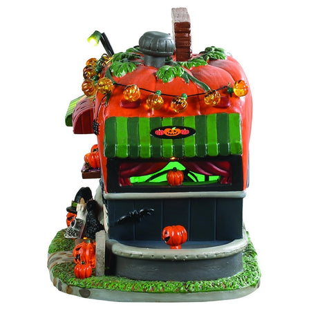 Porcelain lighted building for a Lemax display. Designed to look like a camper made out of a pumpkin. There are carved pumpkins, candles, skulls, spiders, black cats, ghosts and a tombstone. There are lights that are shaped like pumpkins on the roof. There's a sign near the front door that reads "BUY 3 GET ONE FREE!" And a sign on the roof that reads "PICK ME PUMPKIN WAGON."