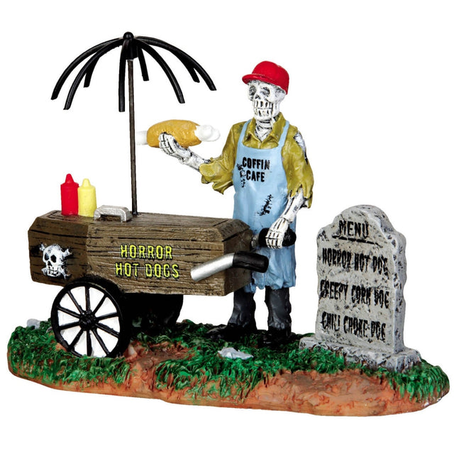 Polyresin figurine for a Lemax Spooky Town display. Designed to look like a skeleton serving hot dogs from a cart. The menu is written on a tombstone.
