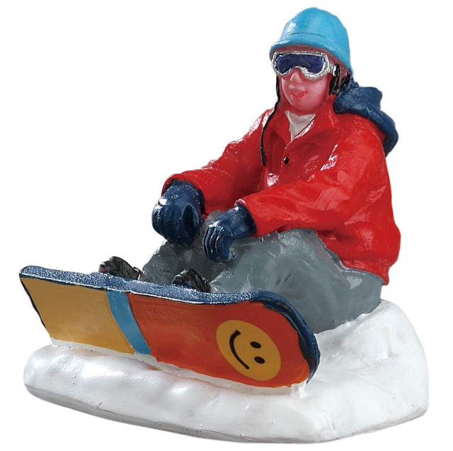 Polyresin figurine for a Lemax Village tabletop display. Designed to look like a man in winter clothes on a snowboard taking a break in the snow.