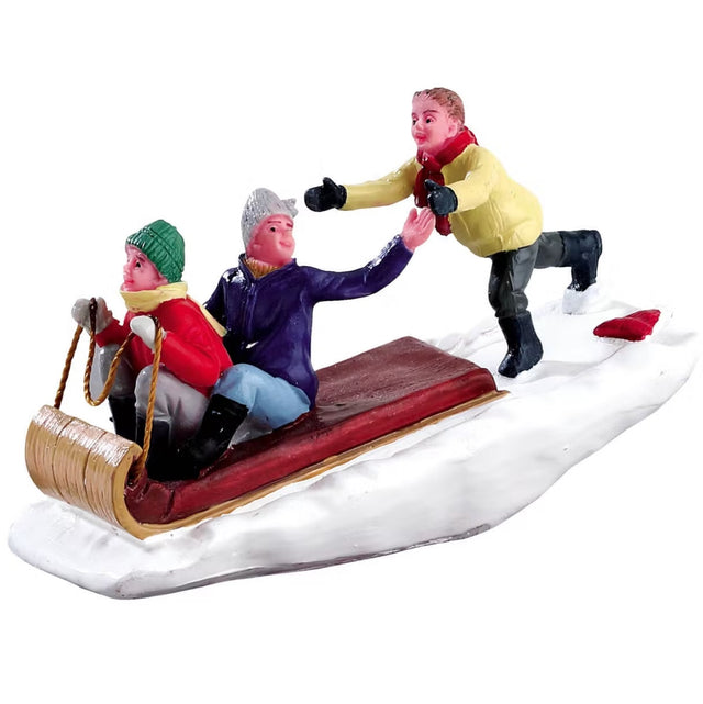 Polyresin figurine for a Lemax display. Designed to look like a young boy chasing after his two friends in a toboggan. They're all wearing winter clothes and the ground is covered in snow.