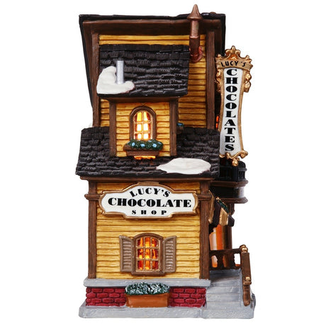 Porcelain lighted building for a Lemax display. Designed to look like an old Victorian-era house with wreaths and snow on it. The house is gold with brown frames. Inside the window you can see an array of chocolates.