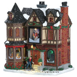 Lemax village building designed to look like an old Victorian style mansion covered in snow. There's green and red tinsel around the roof and some green bushes around the bottom. Scrooge is walking up the front steps.