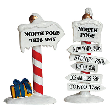 Village accessories for a Lemax display. Designed to look like two directional signs. One reads "NORTH POLE THIS WAY." The other reads "New York 3405, Sydney 8560, London 2261, Los Angeles 3866, Tokyo 3756."