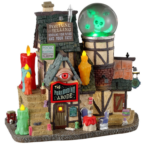 Resin lighted building for a Lemax display. Designed to look like an old-timey cottage. There are colorful candles everywhere. There's an eye above the front door and a giant crystal ball on the roof with a skull, an eye, a broken heart and a moon inside. There's a table outside with two chairs and a crystal ball on the table.