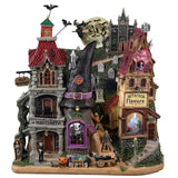 Resin building facade for a Spooky Town Lemax display. Designed to look like a bunch of store fronts. One section is a mortuary with a "help wanted" sign hanging from it. The building next to it reads "NOTION'S POTIONS" and has a witch hat for a roof. The building next to it is a flower shop. Behind them all is a cemetery and a spooky cathedral. There's a witch flying near the moon with bats following behind.
