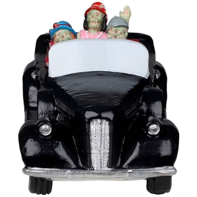Resin village accent for a Lemax Spooky Town display. Designed to look like three people in a shiny, black convertible car. They're all dressed up. The driver is wearing a suit and a gray hat. The woman in the passenger seat is wearing a purple dress and a blue hat. The woman in the backseat is wearing a pink dress, a pearl necklace and a red hat. Their skin is green.