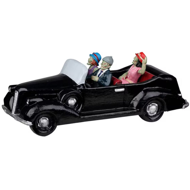 Resin village accent for a Lemax Spooky Town display. Designed to look like three people in a shiny, black convertible car. They're all dressed up. The driver is wearing a suit and a gray hat. The woman in the passenger seat is wearing a purple dress and a blue hat. The woman in the backseat is wearing a pink dress, a pearl necklace and a red hat. Their skin is green.