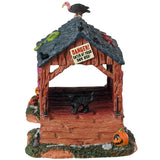 Resin village table accent for a Lemax display. Designed to look like a rotted out, covered bridge. There's a green snake and a vulture on the roof. There's a black cat and a bunch of pumpkins and bones on the ground. There's a sign that reads "DANGER! ENTER AT YOUR OWN RISK!"