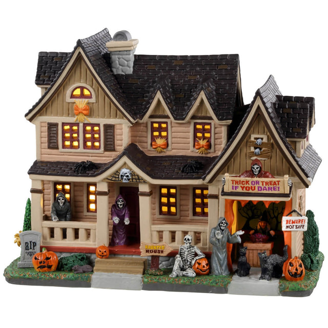 Porcelain lighted building for a Lemax display. Designed to look like a large house with many lit up windows. There are skeletons on the porch, on the front lawn and in the garage. There are also black cats and pumpkins and a little tombstone that reads "RIP."