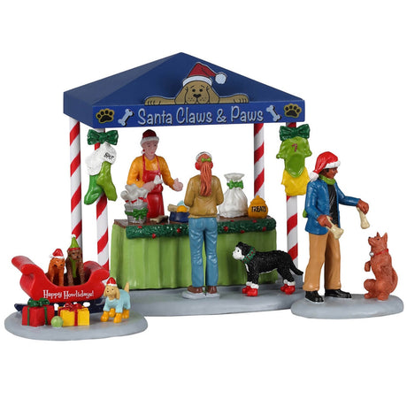 Resin table accent for a Lemax display. Designed to look like a booth that sells pet treats. It's decorated for Christmas. There's a woman handing her dog a bone while another is purchasing some food for her dog who is wearing red booties. There are two dogs wearing Santa hats in a red sleigh posing for pictures.