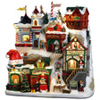 Resin building facade for a Lemax display. Designed to look like a bunch of store fronts decorated for Christmas. The roofs and the sidewalks are covered in snow. There are elves and reindeer and people shopping. There's a window on the left side where you can see Santa inside. There's a work shop, a post office, a sleigh garage, a bakery and some stables.