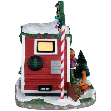 Porcelain lighted building for a Lemax display. Designed to look like a small red and white camper that's selling fresh Christmas trees. There are two people and a puppy checking out some of the trees outside.