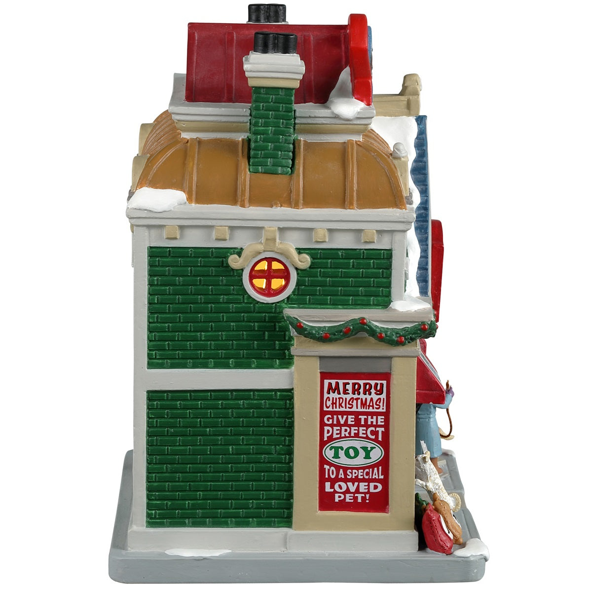 Porcelain lighted building for a Lemax display. Designed to look like a large toy store for pets. There's a white cat looking in the window on the left side of the building and a woman with a dog looking in the window on the right side of the building. There's snow on the roof and the sidewalk. There's a sign that reads "Merry Christmas! Give the perfect toy to a special loved pet!"