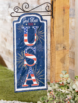 Sign that reads "GOD BLESS THE USA." The background is blue with yellow, white and orange fireworks. The USA is decorated to look like the American flag.