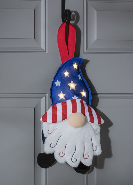 Patriotic hanging decoration designed to look like a gnome with a long, white beard. The gnome is wearing a blue hat with light up stars, the brim of the hat is red and white striped and he's wearing black shoes.