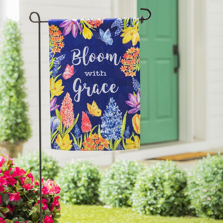 A royal blue flag that reads "Bloom with Grace" and features a bunch of different colored flowers and butterflies in a garden in front of a house