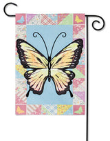 A flag featuring an Ornythion Swallowtail Butterfly. The background of this flag consists of different looking and different colored materials. Colors include: red, pink, yellow, light blue, lime green and orange