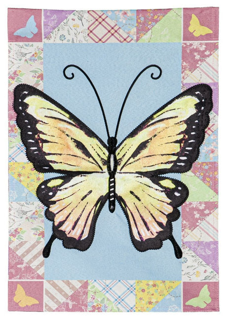 A flag featuring an Ornythion Swallowtail Butterfly. The background of this flag consists of different looking and different colored materials. Colors include: red, pink, yellow, light blue, lime green and orange
