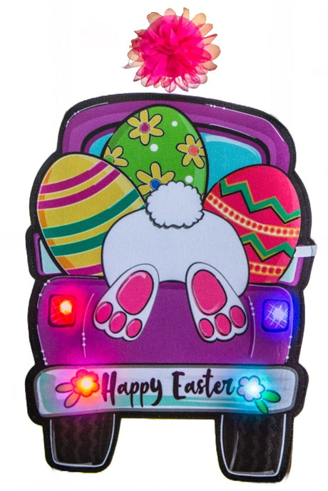 A mat for your front door that reads "Happy Easter" and features a cute bunny butt sticking out of the back of a pink truck carrying three multi-colored eggs. The lights on the truck and the flowers on the bumper light up