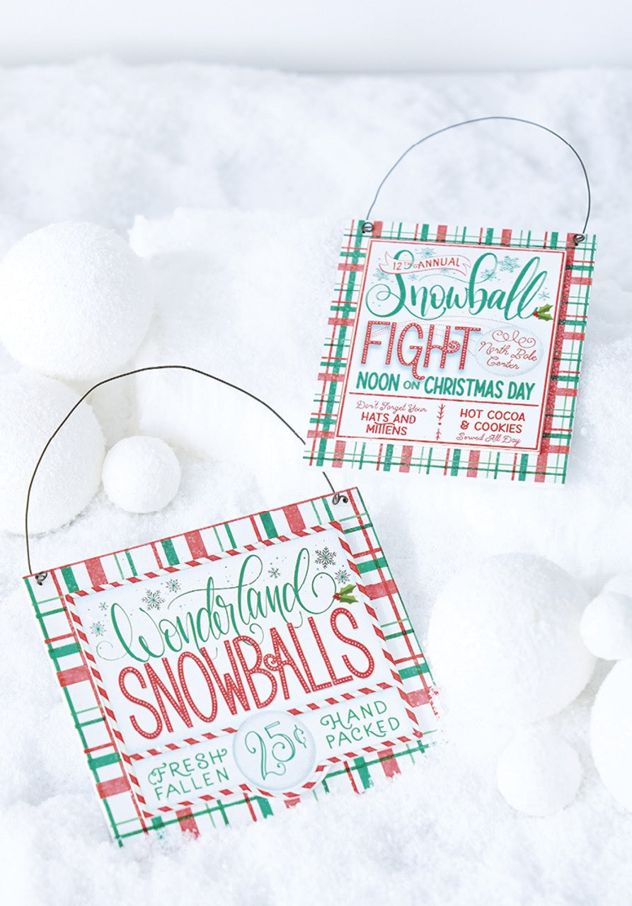 Both of the signs are resting among fake snow and fake snowballs.