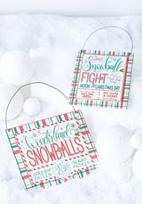 Both of the signs are resting among fake snow and fake snowballs.