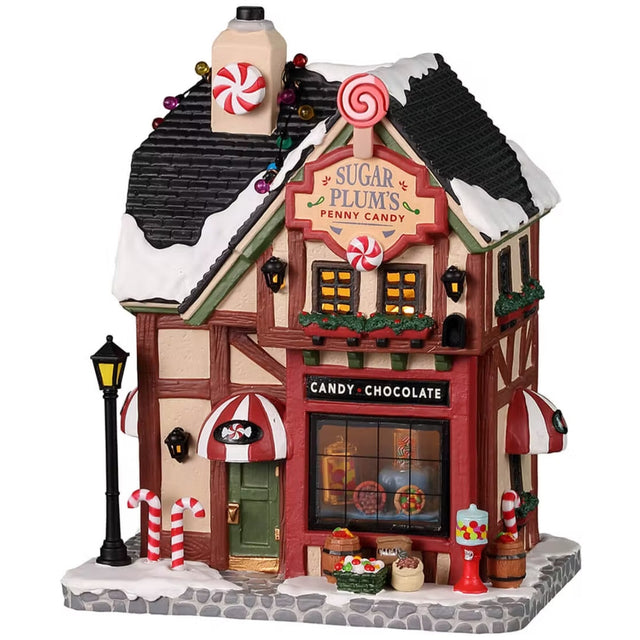 Porcelain lighted building for a Lemax display. Designed to look like a candy shop. There's snow on the roof and the sidewalk. Inside the window, you can see a bunch of candy on display. In front of the shop, there are peppermint candy canes, baskets of candy and a bubblegum machine.