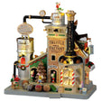 Polyresin lighted building for a Lemax display. Designed to look like a Christmas themed factory. There's an elf sitting on top of the roof. Signs read "Milk Chocolate," "Dark Chocolate," "Truffle Factory, "Kitchen" and "Chocolate." There's a display of truffles in the front window and a bunch of elves working hard.