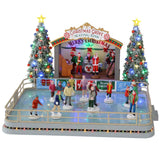 Plastic, animated figure for a Lemax display. Designed to look like an ice skating rink. There are a bunch of people skating around. There's a band on the stage in Christmas outfits and Santa hats. The sign on the stage reads "Christmas Grove Skating Rink. Merry Christmas." There are two tall, decorated Christmas trees on either side of the stage.