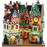 Polyresin building facade for a Lemax display. Designed to look like a collection of store fronts that are decorated for Christmas. Santa is in the front window of one of the stores. There's a person sitting outside of the Wine Bar.