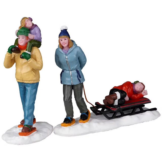 Resin figurines for a Lemax display. One figure is a man holding a young child on his shoulders. The other figure is a mom puling a sled with another young child laying on it. They're all wearing winter clothes and the ground is snow.