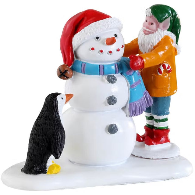 Resin figure for a Lemax display. Designed to look like an elf putting a scarf on a snowman. The snowman is wearing a Santa hat. A little penguin is standing nearby.