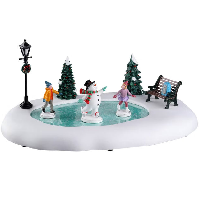 Plastic village accent for a Lemax display. Designed to look like two kids ice skating with Frosty the Snowman. There's a bench with a blue backpack on it. There are two snow-covered trees and a lamppost with a decorated wreath on it.