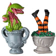 Resin village accessories for a Lemax Spooky Town display. Designed to look like plants in planters. One is a Venus fly trap plant in a blue-gray pot. The other is a pair of witch legs coming out of green leaves in a tan pot. The legs are wearing black and orange tights with black boots.