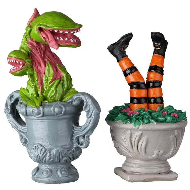 Resin village accessories for a Lemax Spooky Town display. Designed to look like plants in planters. One is a Venus fly trap plant in a blue-gray pot. The other is a pair of witch legs coming out of green leaves in a tan pot. The legs are wearing black and orange tights with black boots.