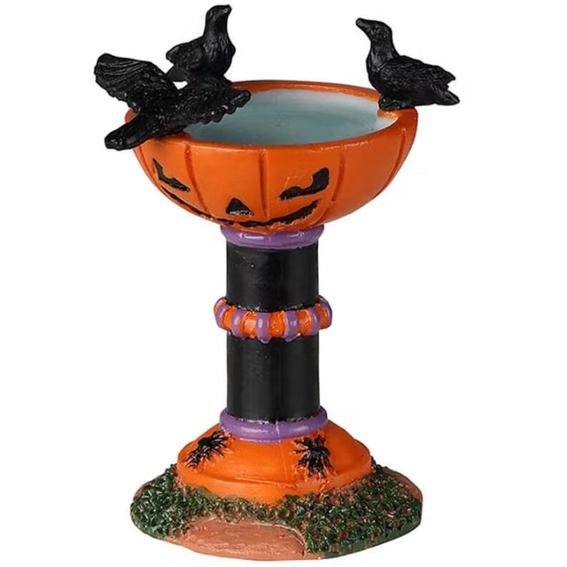 Resin village accessory for a Lemax Halloween display. Designed to look like a bird bath with three birds sitting on the rim. The top of the bird bath looks like a carved pumpkin. The base of the bird bath is black, purple and orange and has spiders on it.