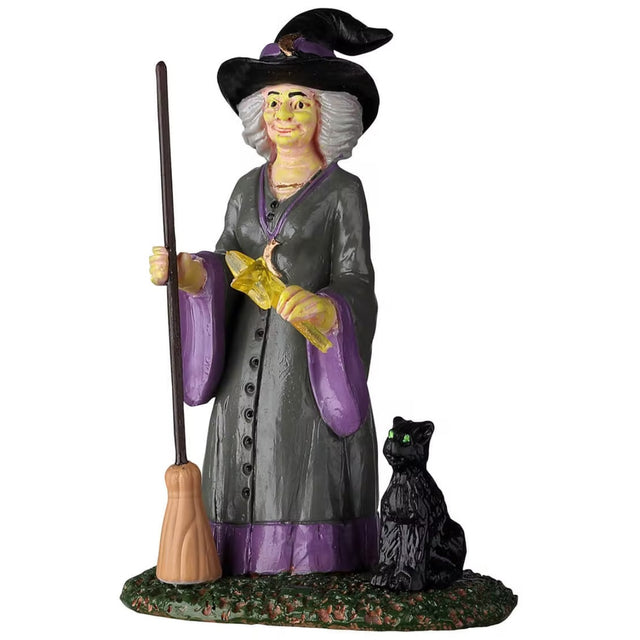 Polyresin figurine for a Spooky Town Lemax display. Designed to look like a witch holding a broom and a yellow wand with a star on it. There's a black cat sitting next to her. The witch is wearing a black witch hat and a gray and purple robe. The witch has short, white hair.