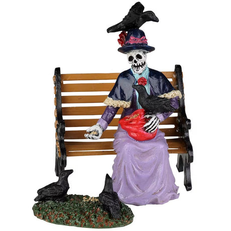 Resin figurine for a Lemax Spooky Town display. Designed to look like a female skeleton sitting on a wooden bench feeding a bunch of crows. Her dress is purple, she's wearing a top hat with a crow standing on top.