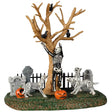 Resin village accent for a Lemax display. Designed to look like a skeleton dancing in a graveyard. There are tombstones and carved pumpkins on the grass. There's also a bare tree with crows on the branches. There are also skeleton dogs.