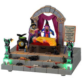 Polyresin village accent for a Lemax display. Designed to look like two witches doing magic on an altar. The altar has gargoyle statues, rats, bottles of potions, blood and bones. The witches are levitating a woman off the table. The table is shaped like a coffin. There's a boiling cauldron next to them and there's a crow sitting on it.